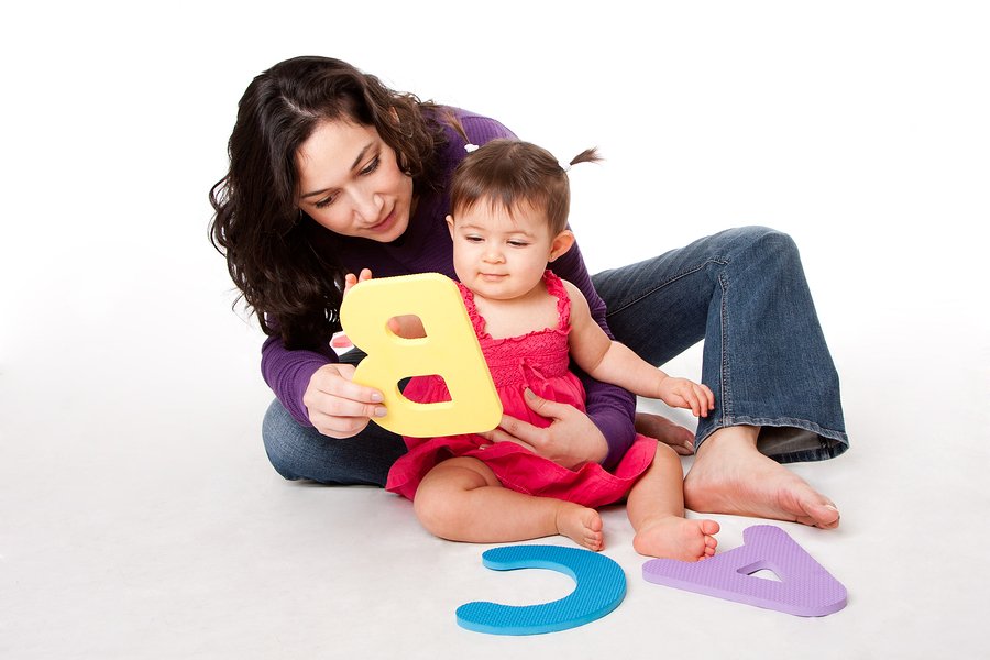 Mother nanny or teacher teaching happy baby to learn alphabet A B C with letters in a playful way while sitting on floor.